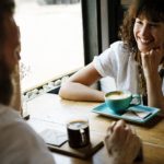Mulher sorrindo enquanto conversa com um homem em uma cafeteria.