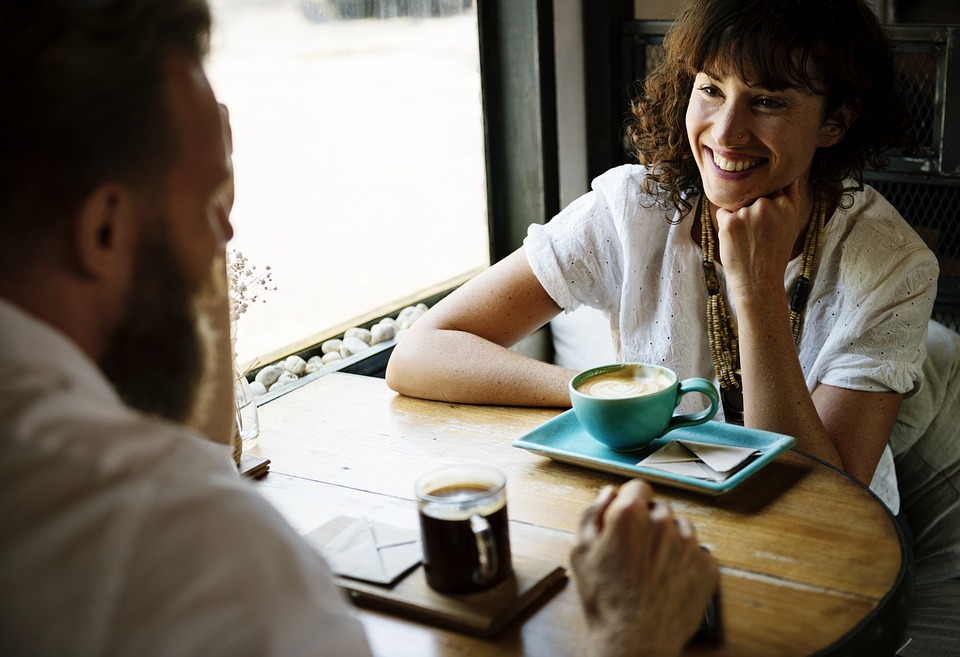 Mulher sorrindo enquanto conversa com um homem em uma cafeteria.