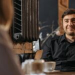 Homem sorrindo enquanto conversa em um café, demonstrando atenção e acolhimento.
